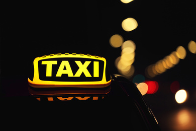 Photo of Taxi car with yellow roof sign on city street at night, closeup