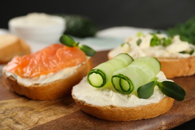 Photo of Delicious sandwiches with cream cheese and other ingredients on wooden board, closeup