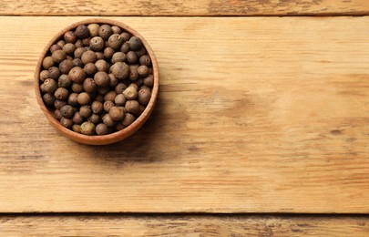 Photo of Dry allspice berries (Jamaica pepper) in bowl on wooden table, top view. Space for text