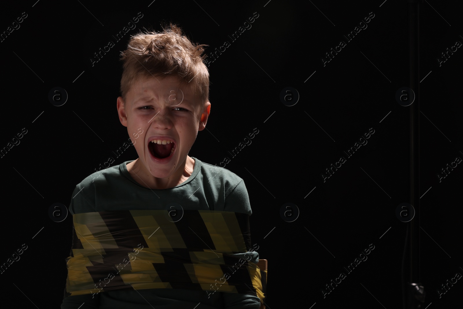 Photo of Scarred little boy tied up and taken hostage on dark background. Space for text