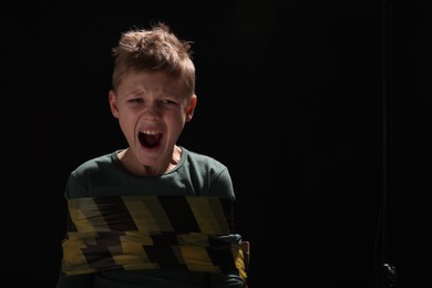 Photo of Scarred little boy tied up and taken hostage on dark background. Space for text