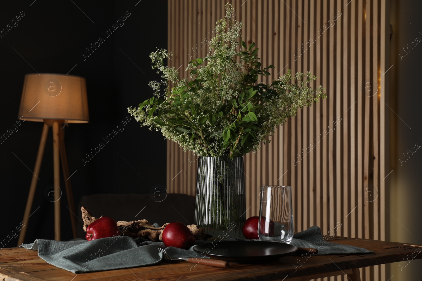 Photo of Set of clean dishware, ripe red apples and flowers on wooden table in stylish dining room