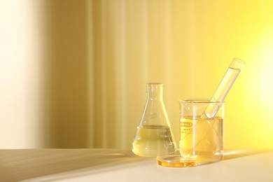 Photo of Laboratory analysis. Different glassware on table against light yellow background, space for text