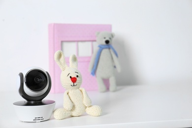 Photo of Baby camera with toys and photo album on table against white background, space for text. Video nanny