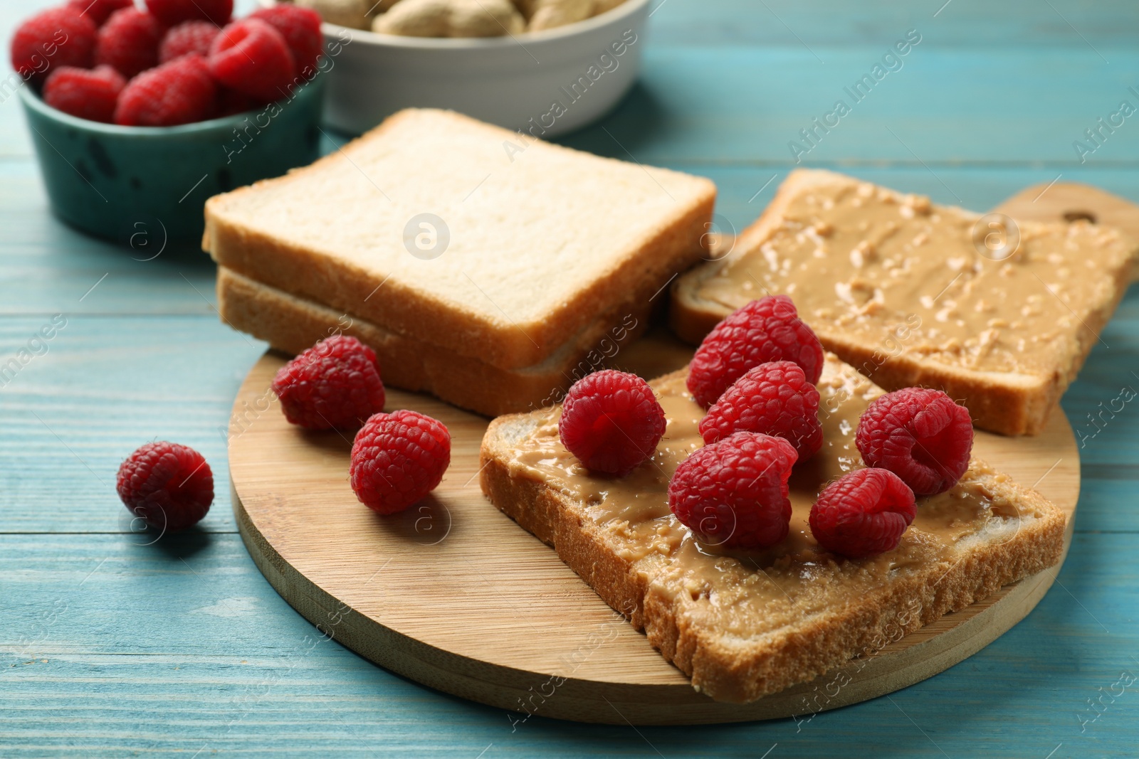 Photo of Delicious toasts with peanut butter and raspberries on light blue wooden table, closeup