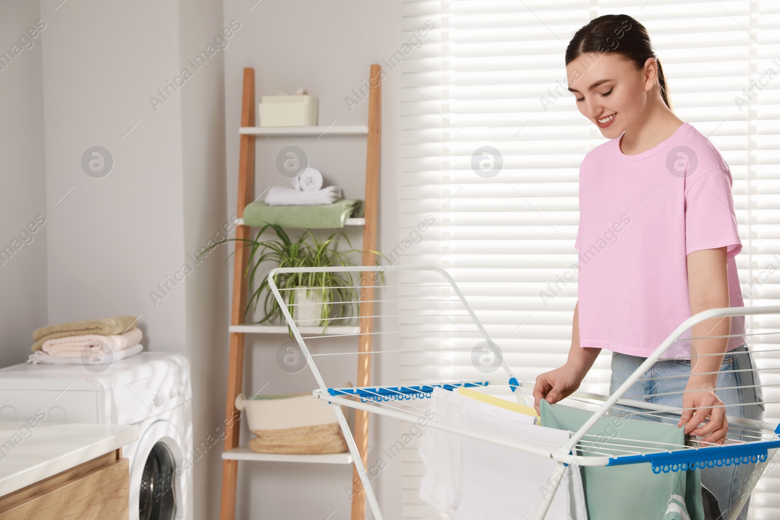 Photo of Woman hanging different apparel on clothes airer in bathroom