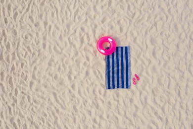 Striped beach towel, flip flops and swim ring on sand, aerial view. Space for text
