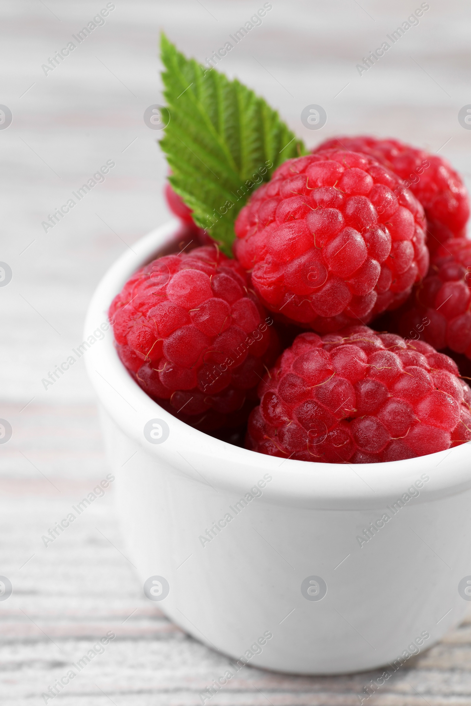 Photo of Tasty ripe raspberries and green leaf on white wooden table, closeup