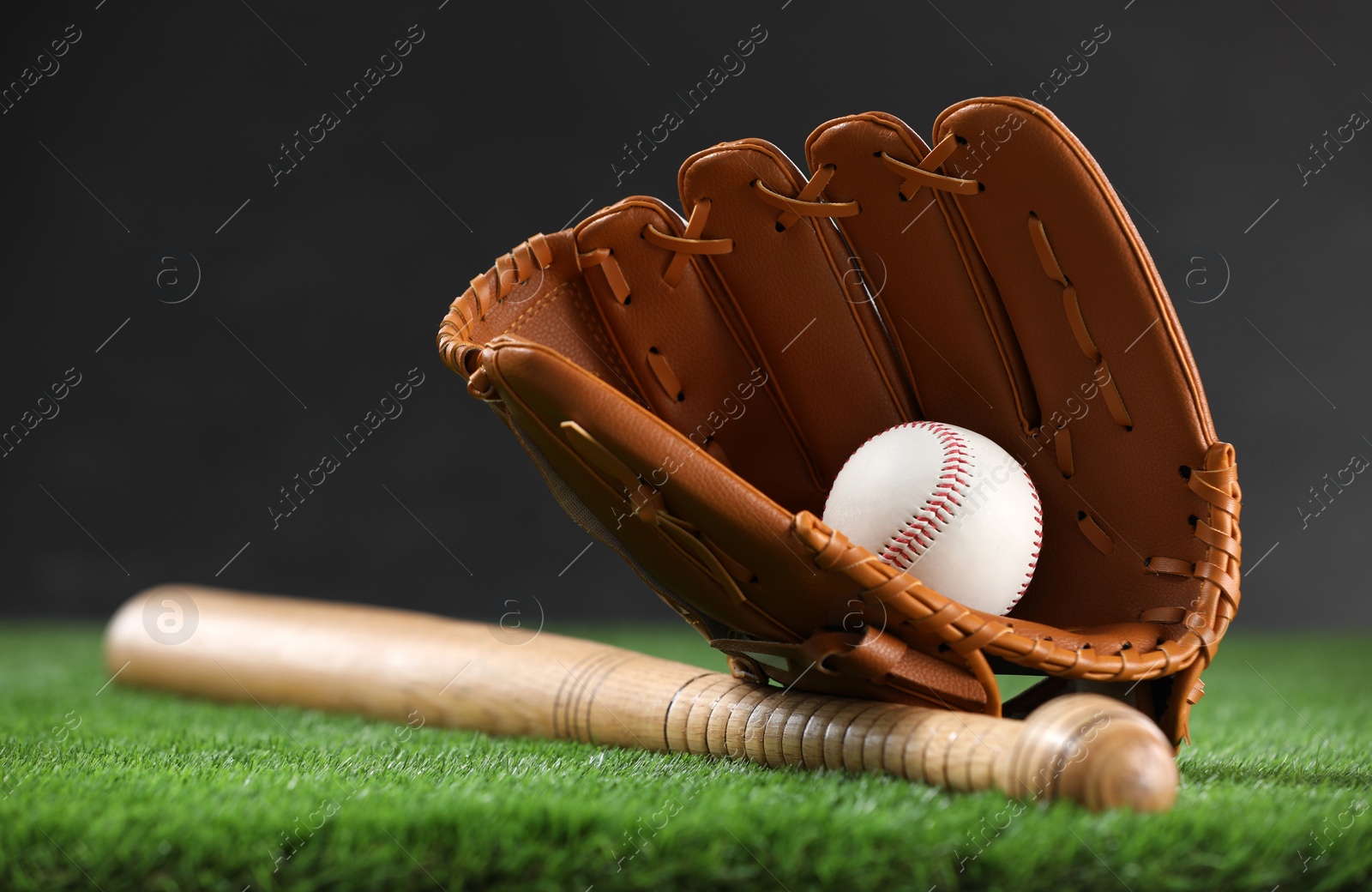 Photo of Baseball bat, leather glove and ball on green grass against dark background, closeup