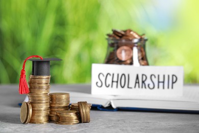 Photo of Scholarship concept. Coins and graduation cap on grey table, space for text