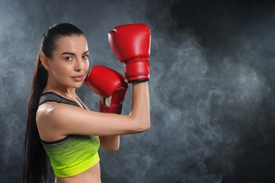 Photo of Beautiful woman wearing boxing gloves training in smoke on black background. Space for text