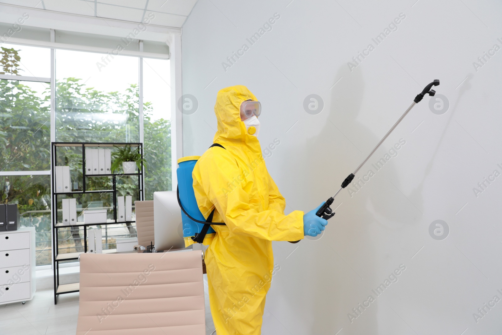 Photo of Janitor in protective suit disinfecting office to prevent spreading of COVID-19