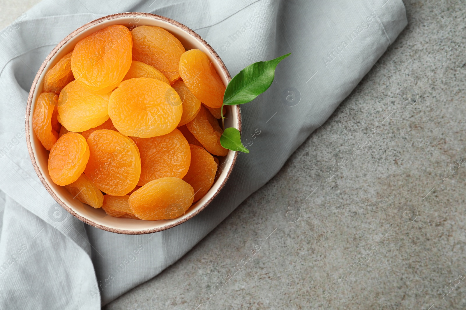 Photo of Bowl of tasty apricots and space for text on grey table, top view. Dried fruits