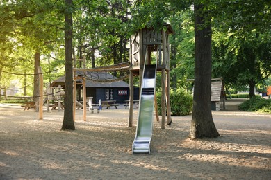 Photo of Outdoor playground with wooden slide near big trees in park