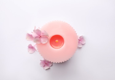 Burning pink wax candle and flowers isolated on white, top view