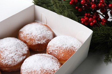 Photo of Delicious sweet buns in box, fir tree branches and red berries on table, closeup