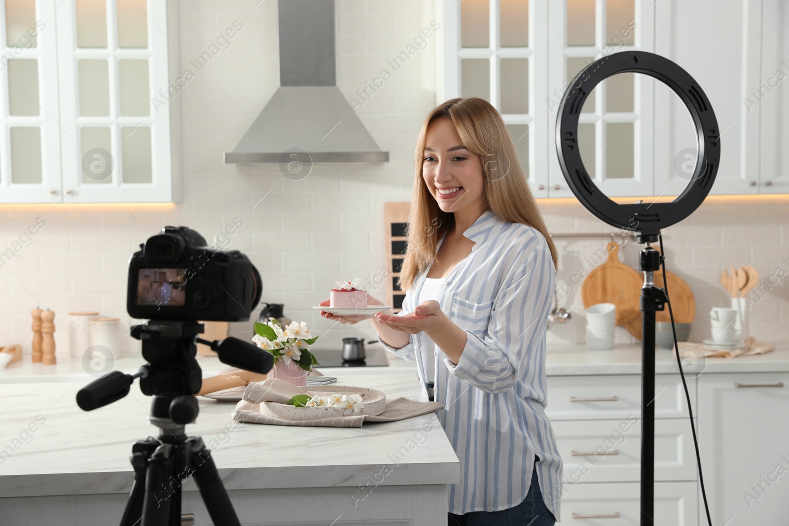 Photo of Blogger with tasty cake recording video in kitchen at home. Using ring lamp and camera