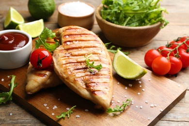 Photo of Tasty grilled chicken fillets with tomato and lime on wooden board, closeup