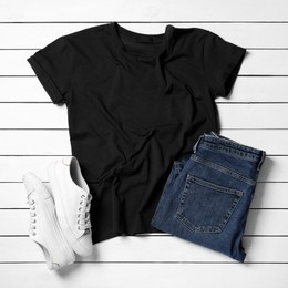 Stylish t-shirt, jeans and sneakers on white wooden background, flat lay