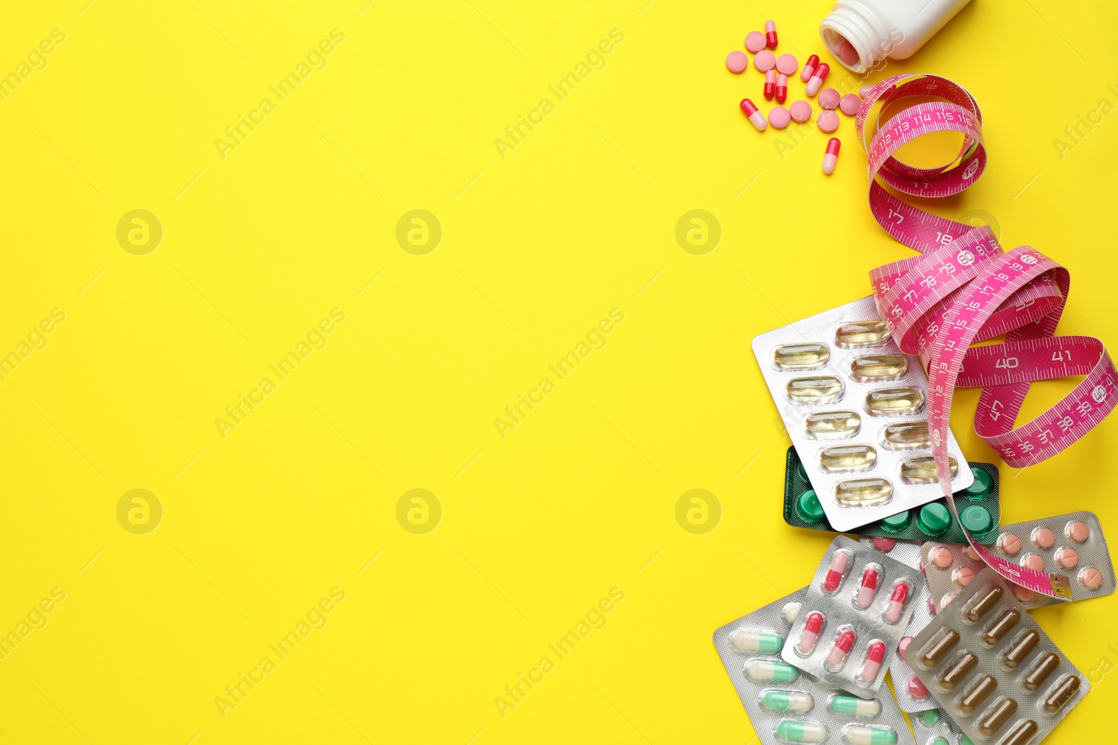 Photo of Weight loss pills and measuring tape on yellow background, flat lay. Space for text