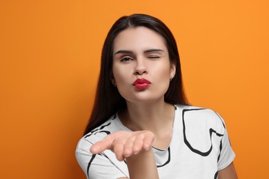 Photo of Beautiful young woman blowing kiss on orange background