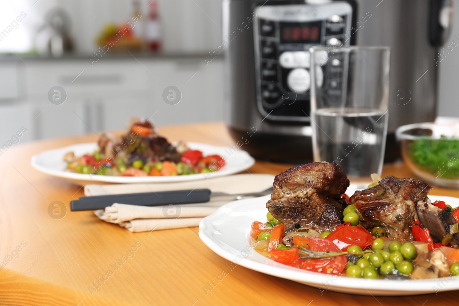 Photo of Plate with meat and garnish prepared in multi cooker on wooden table in kitchen. Space for text