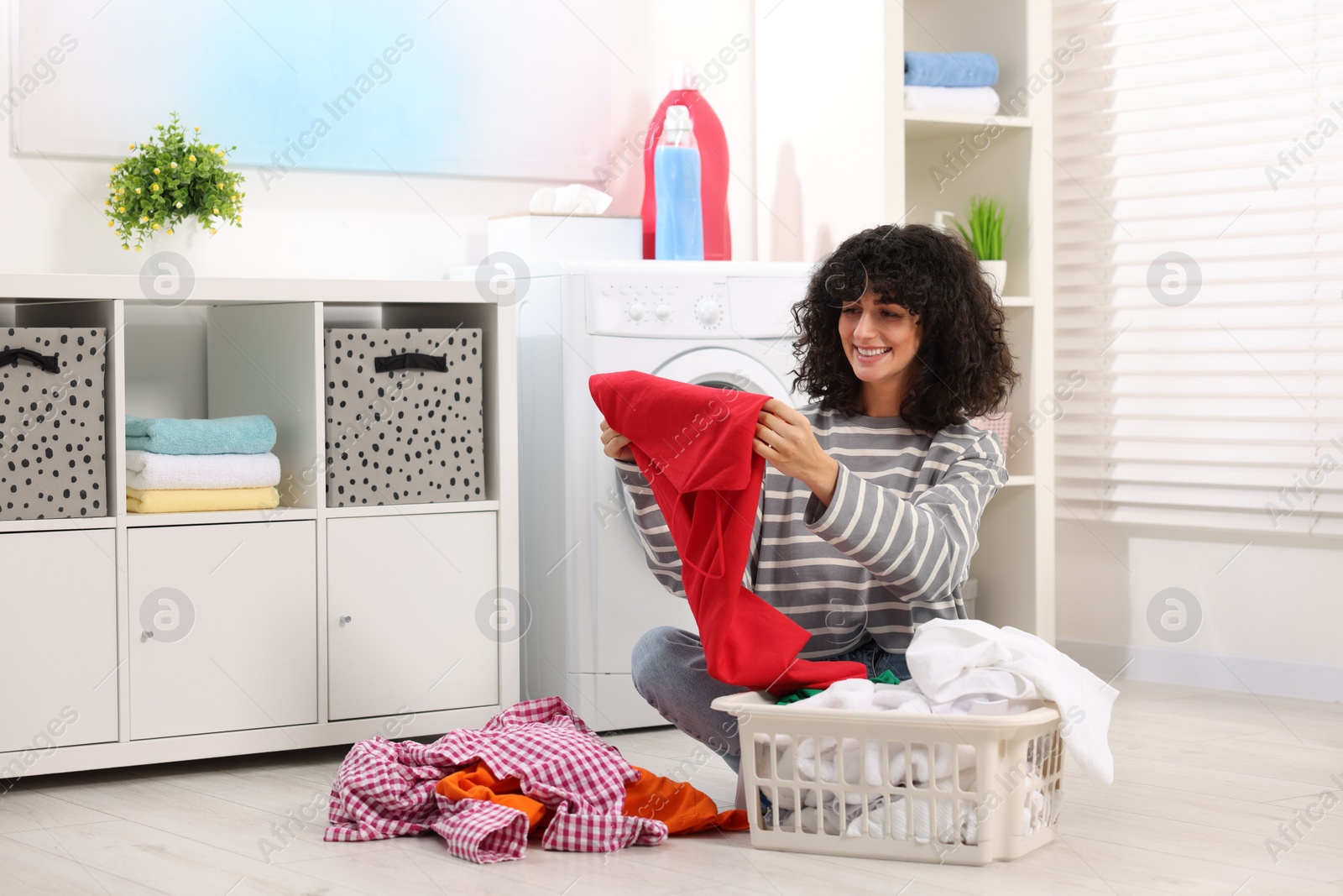 Photo of Happy woman with laundry near washing machine indoors