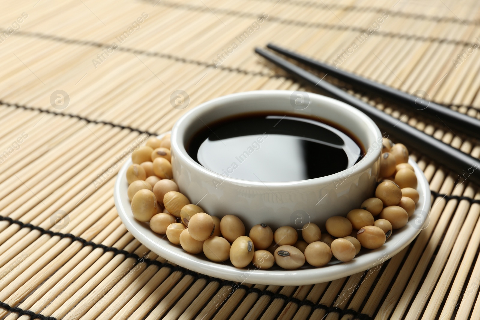 Photo of Dish of soy sauce with beans and chopsticks on bamboo mat