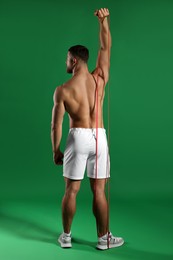 Photo of Muscular man exercising with elastic resistance band on green background, back view