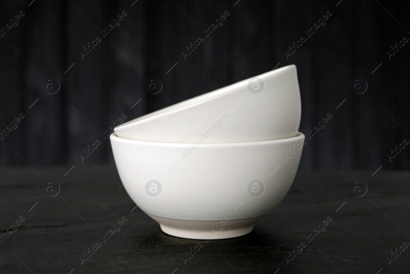 Photo of Stylish empty ceramic bowls on black table. Cooking utensils