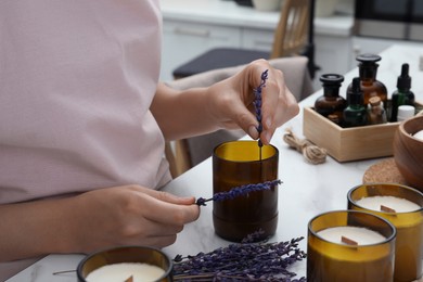 Photo of Woman decorating homemade candle with lavender flowers at table indoors, closeup
