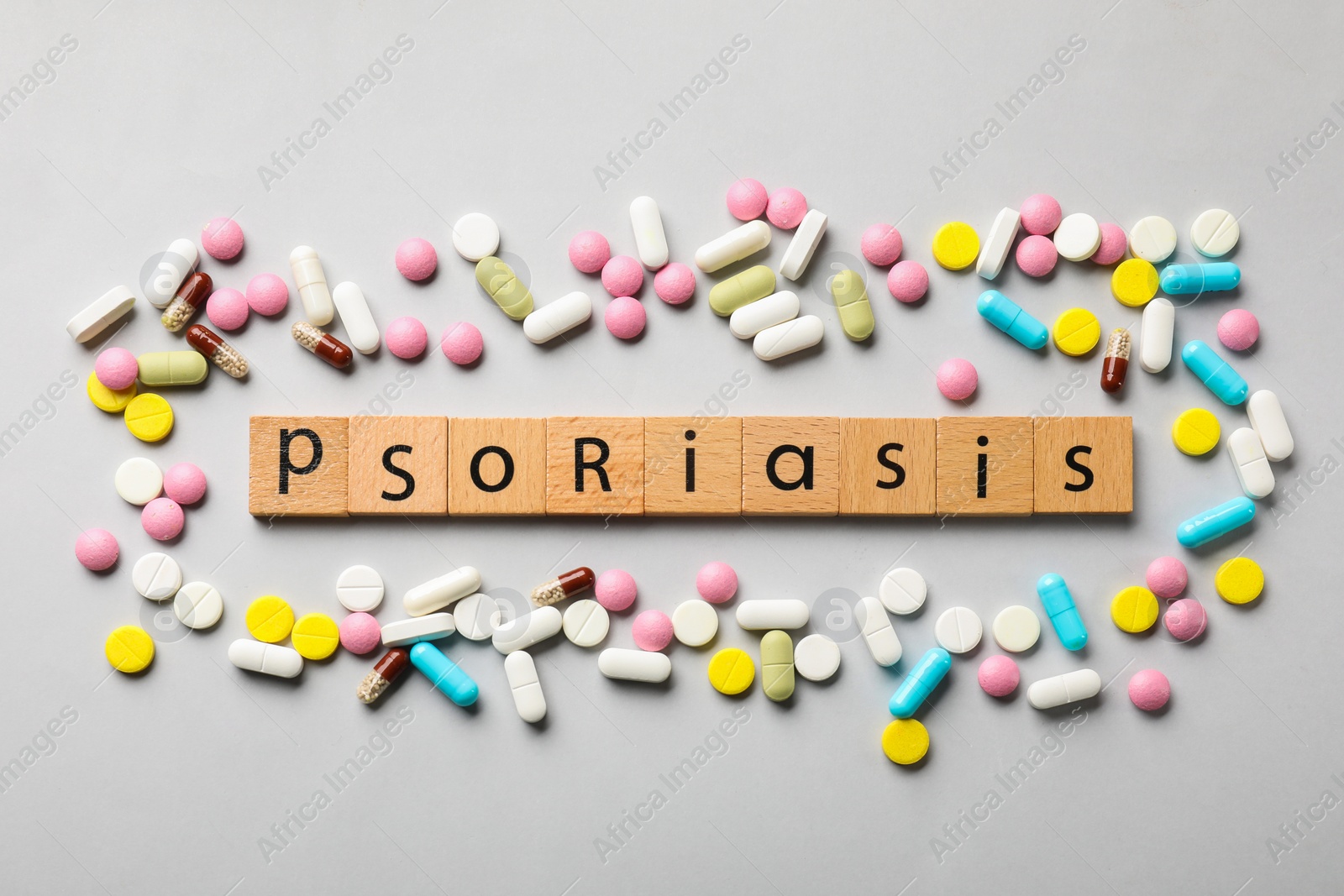 Photo of Word Psoriasis made of wooden squares with letters and different pills on light grey background, flat lay