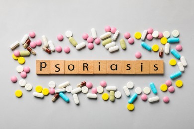 Photo of Word Psoriasis made of wooden squares with letters and different pills on light grey background, flat lay