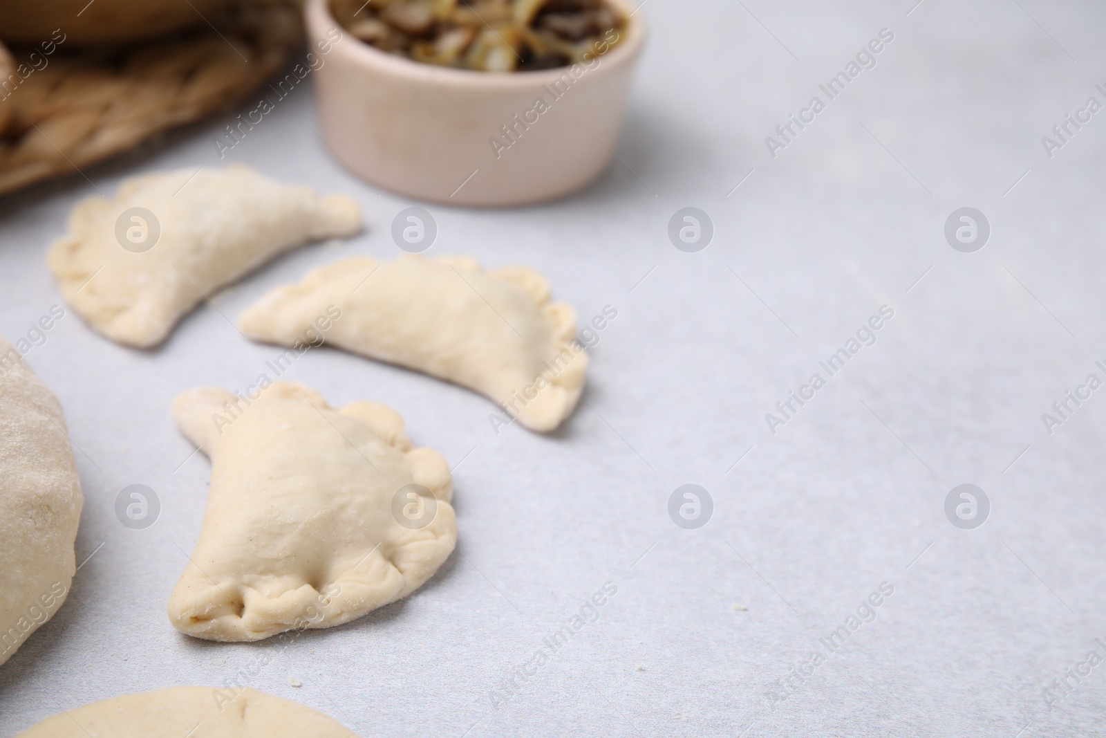 Photo of Process of making dumplings (varenyky) with mushrooms. Raw dough and ingredients on white table, closeup. Space for text