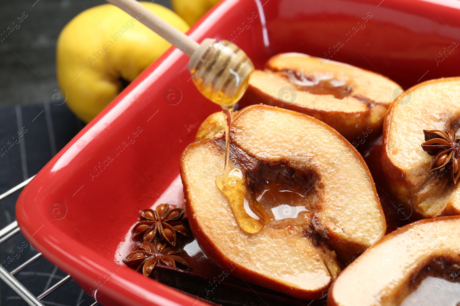 Photo of Pouring tasty honey onto baked quinces in dish on table, closeup