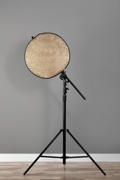 Professional golden reflector on tripod near grey wall in room. Photography equipment
