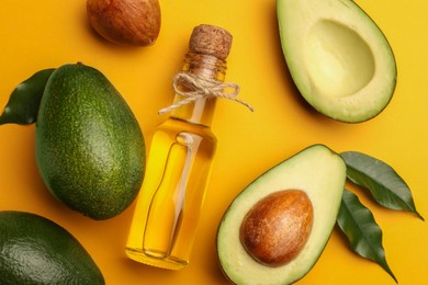 Photo of Glass bottle of cooking oil and fresh avocados on yellow background, flat lay