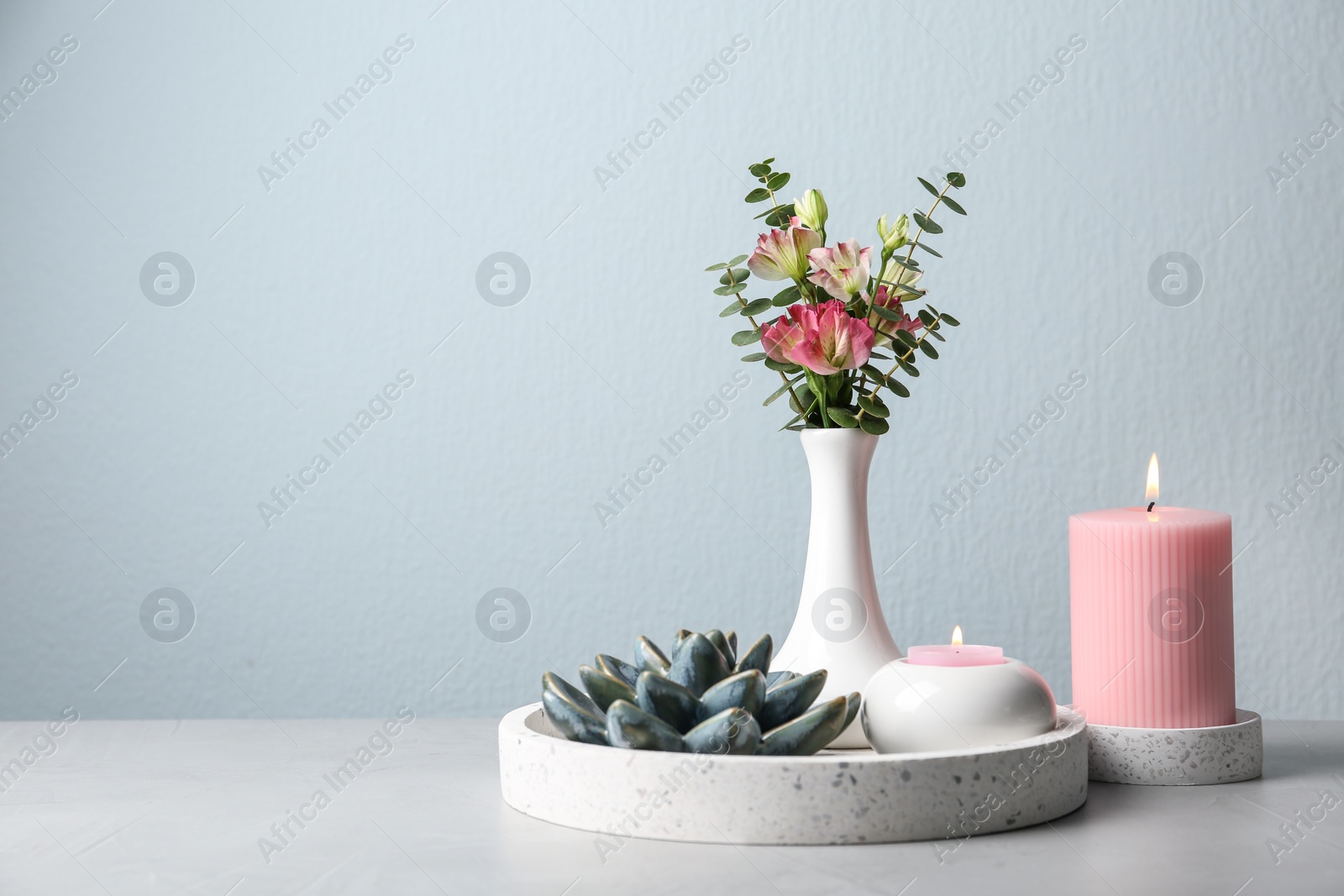 Photo of Stylish tender composition with burning candles and flowers on white table against light background, space for text. Cozy interior element