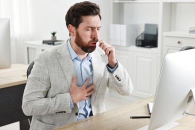 Photo of Sick man with tissue coughing at workplace in office