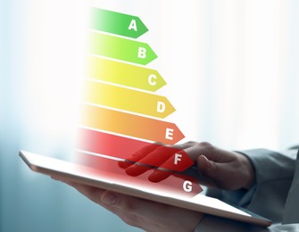 Energy efficiency rating coming out of tablet. Man using device on light background, closeup