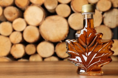 Leaf shaped bottle of tasty maple syrup on wooden table, space for text