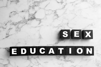 Black wooden blocks with phrase "SEX EDUCATION" on marble background, flat lay