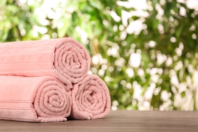 Photo of Rolled towels on wooden table against blurred background, space for text