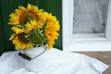 Bouquet of beautiful sunflowers in tin on wooden table near window outdoors