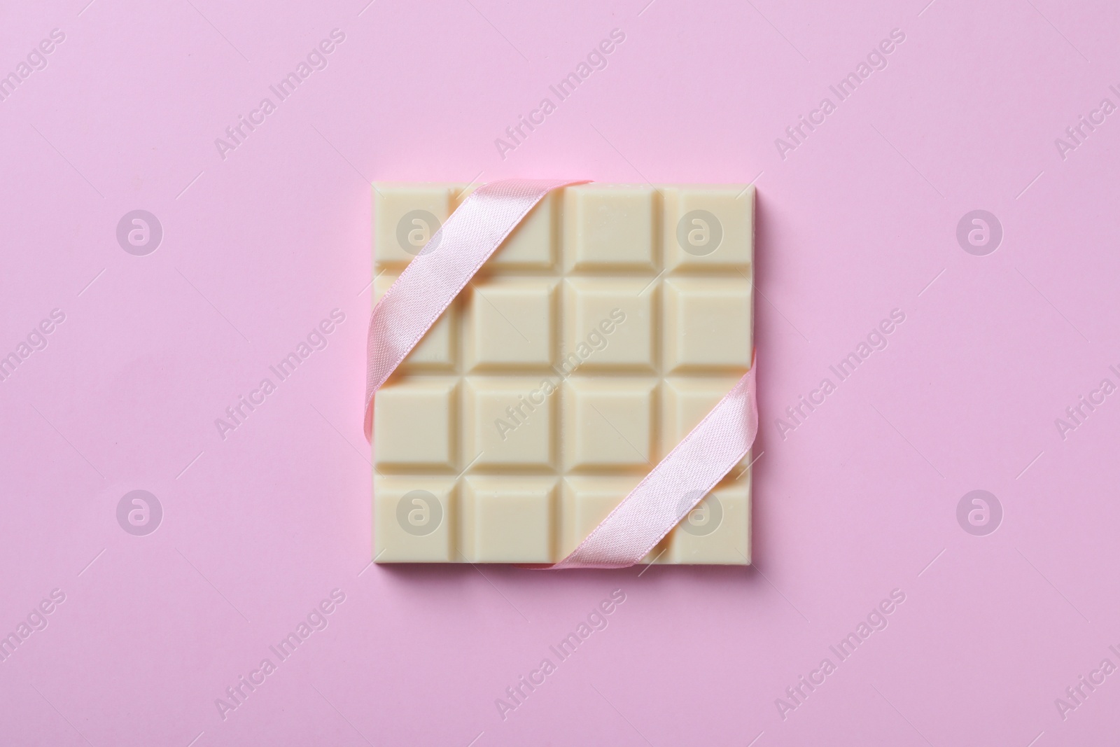 Photo of Tasty white chocolate bar with ribbon on pink background, top view