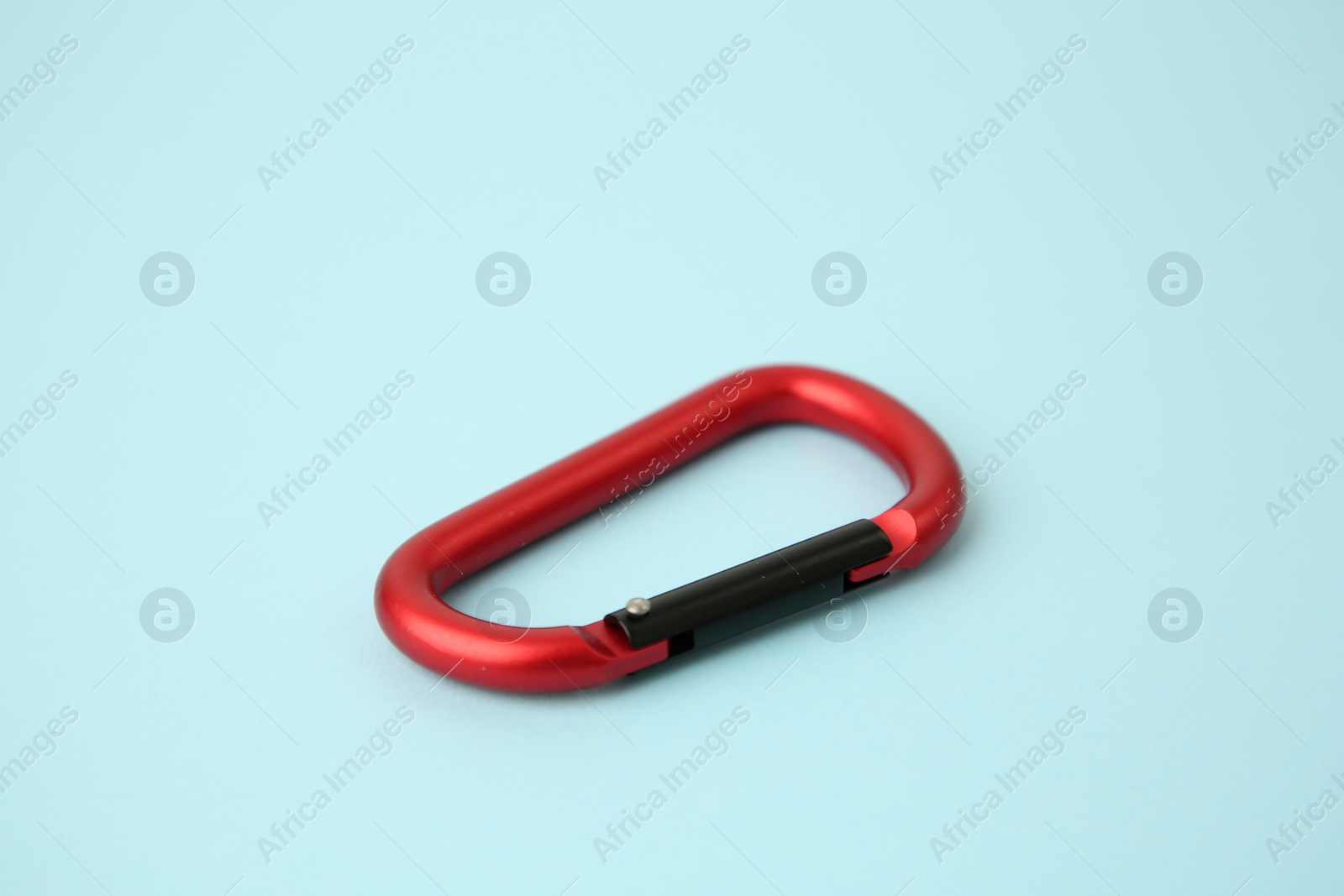 Photo of One red carabiner on light blue background, closeup