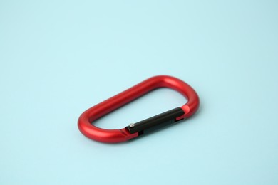 One red carabiner on light blue background, closeup