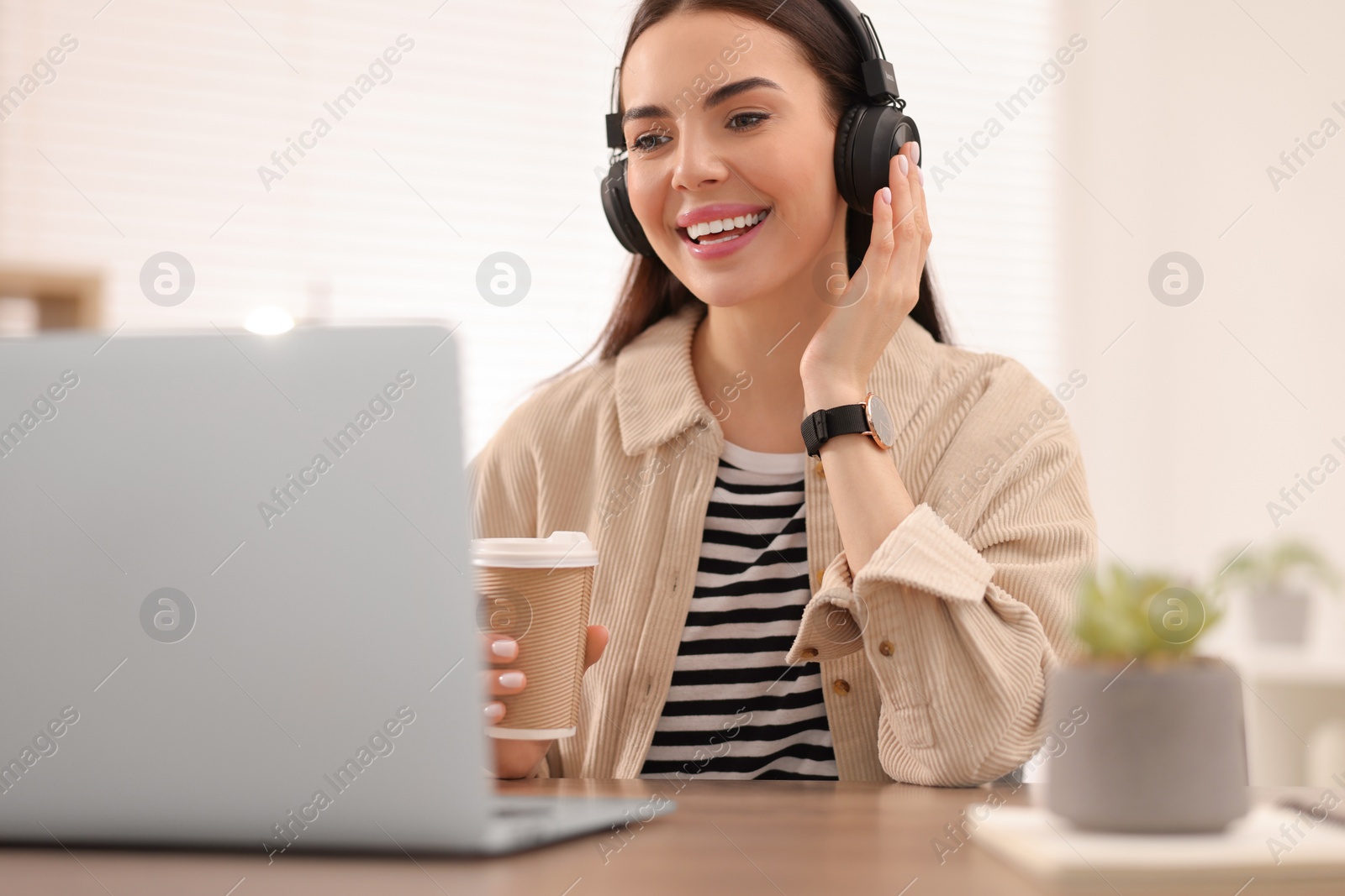 Photo of Young woman in headphones watching webinar at table in room