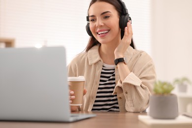 Young woman in headphones watching webinar at table in room