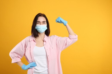 Photo of Woman with protective mask and gloves showing muscles on yellow background, space for text. Strong immunity concept